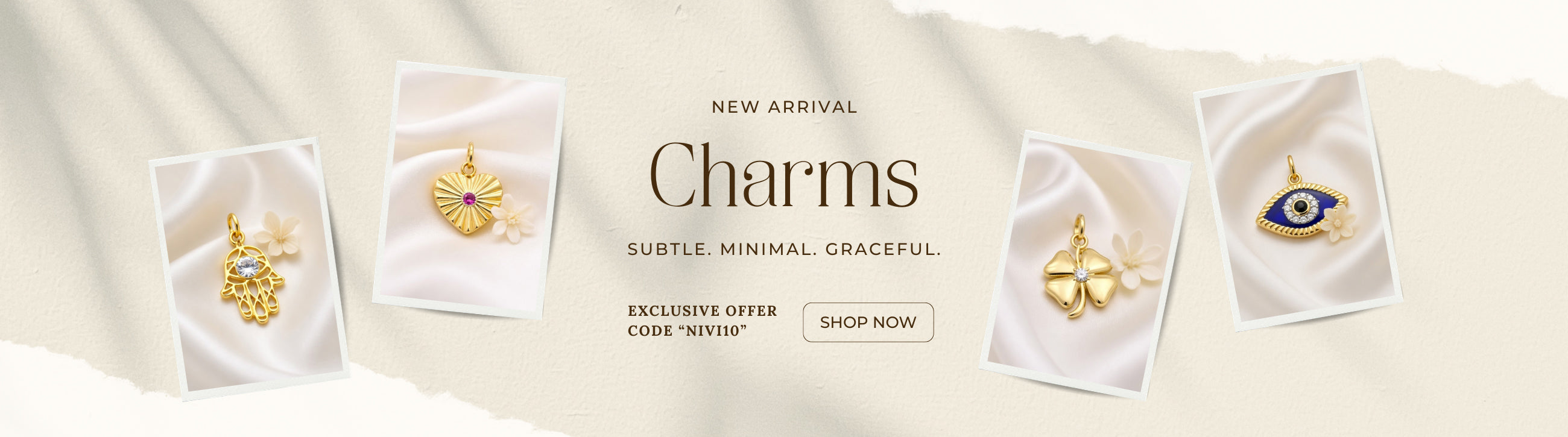Homepage banner showcasing NIVI's Charms Collection featuring four handcrafted charm pendants displayed on elegant satin-inspired cards against a soft ivory background. The collection includes a Hamsa hand charm, radiant heart charm, four-leaf clover charm, and evil eye charm, crafted in 925 sterling silver with one-micron gold plating. The banner highlights the message "New Arrival – Charms" with the tagline "Subtle. Minimal. Graceful." and features an exclusive offer code "